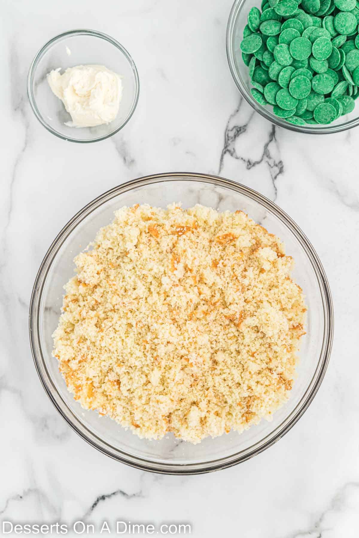 Bake cake crumbled in a bowl with a small bowl of green candy melts and frosting