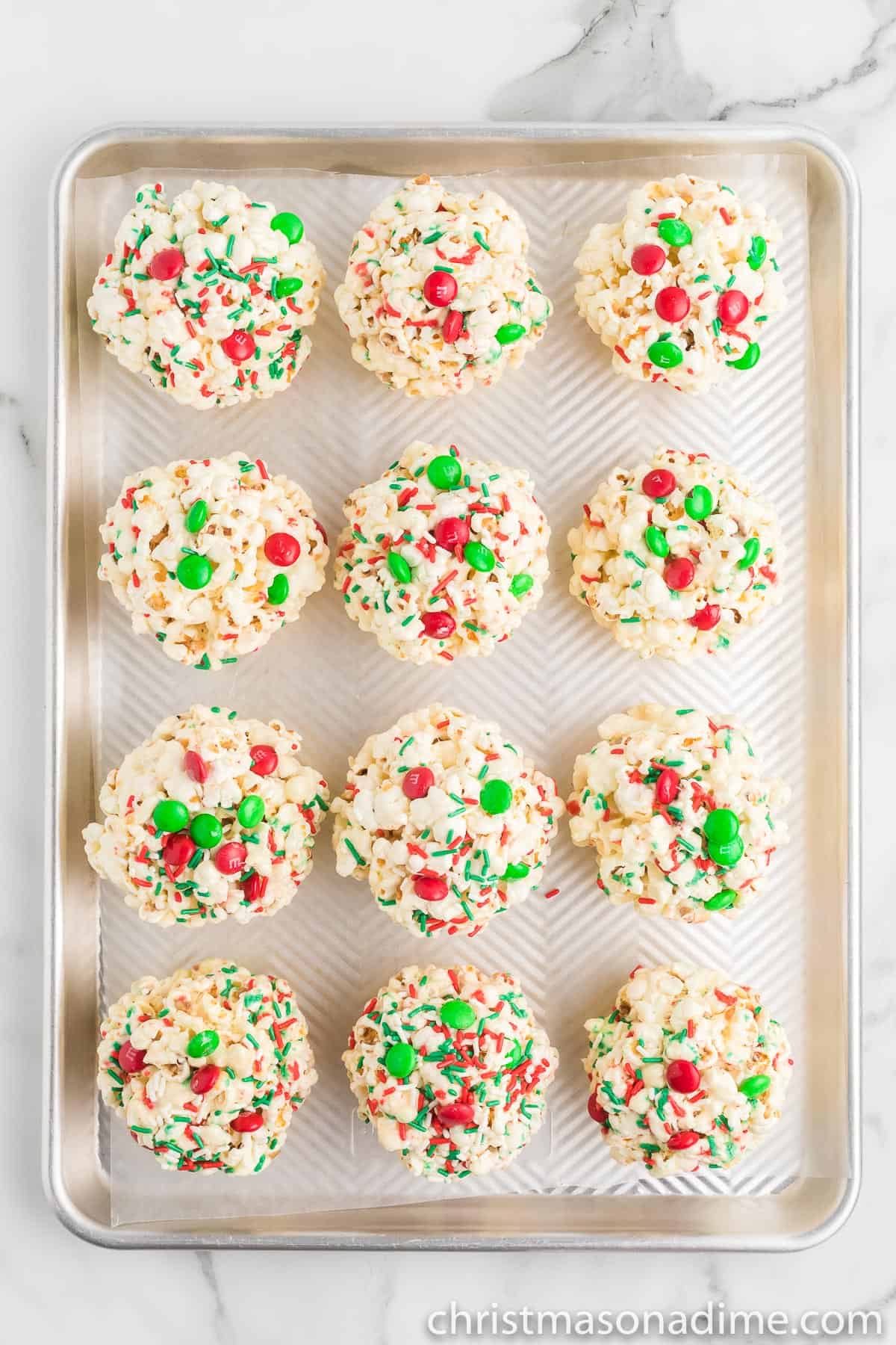 Christmas Popcorn Balls placed on a baking sheet with red and green sprinkles and M&Ms
