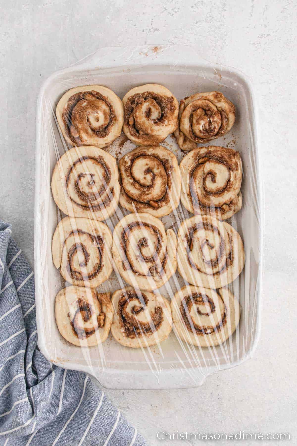 Cinnamon roll dough in a baking dish covered with plastic wrap