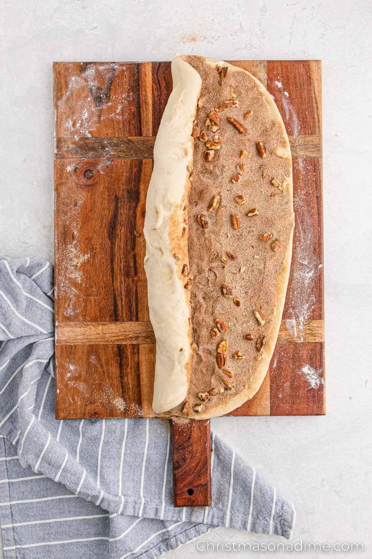 Rolling the dough with the cinnamon sugar mixture with chopped nuts on a floured surface