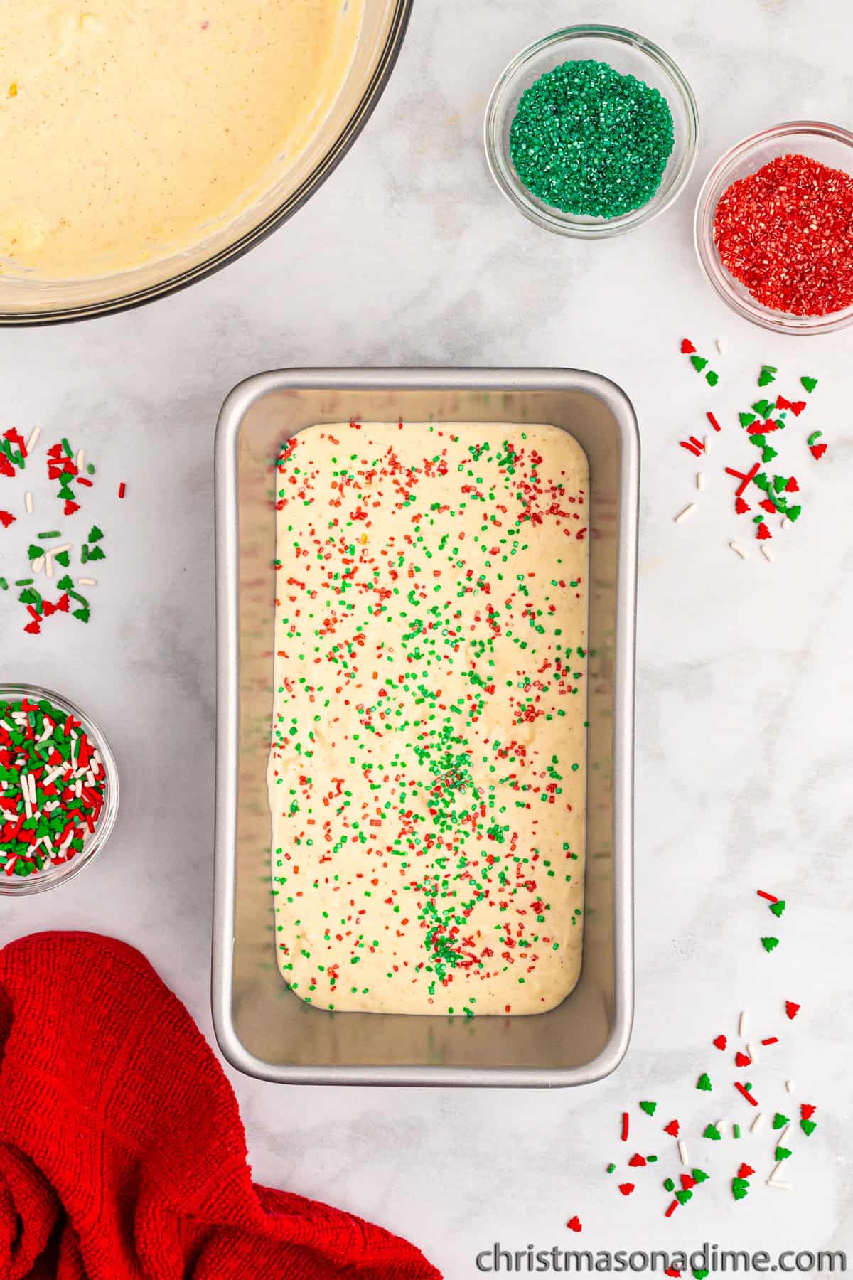 Topping the heavy cream with red and green sprinkles in a loaf pan