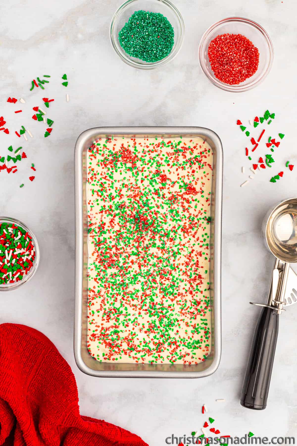 Ice cream mixture in a loaf pan topped with red and green sprinklnes