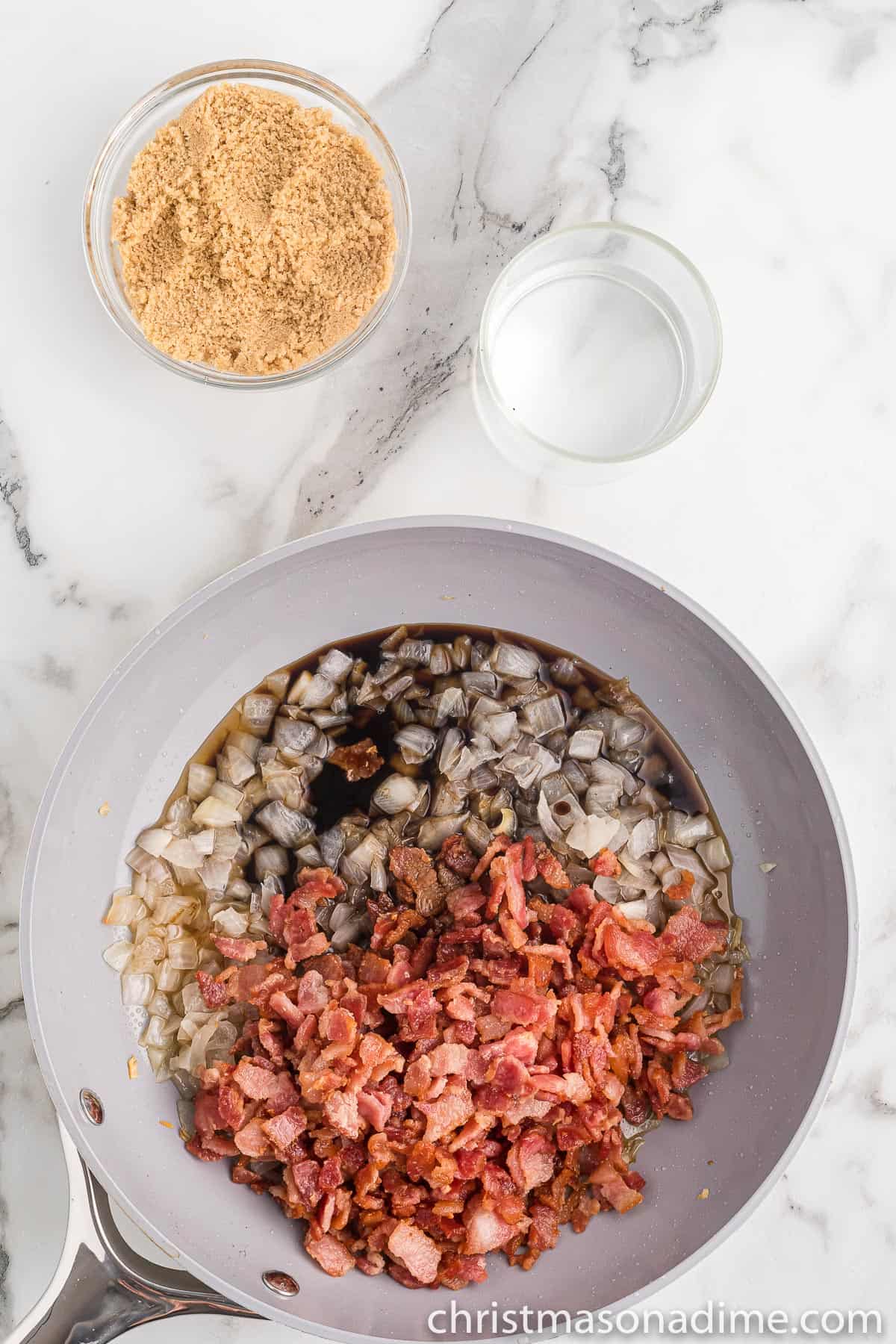 Chopped cooked bacon in a skillet with chopped onions topped with vinegar