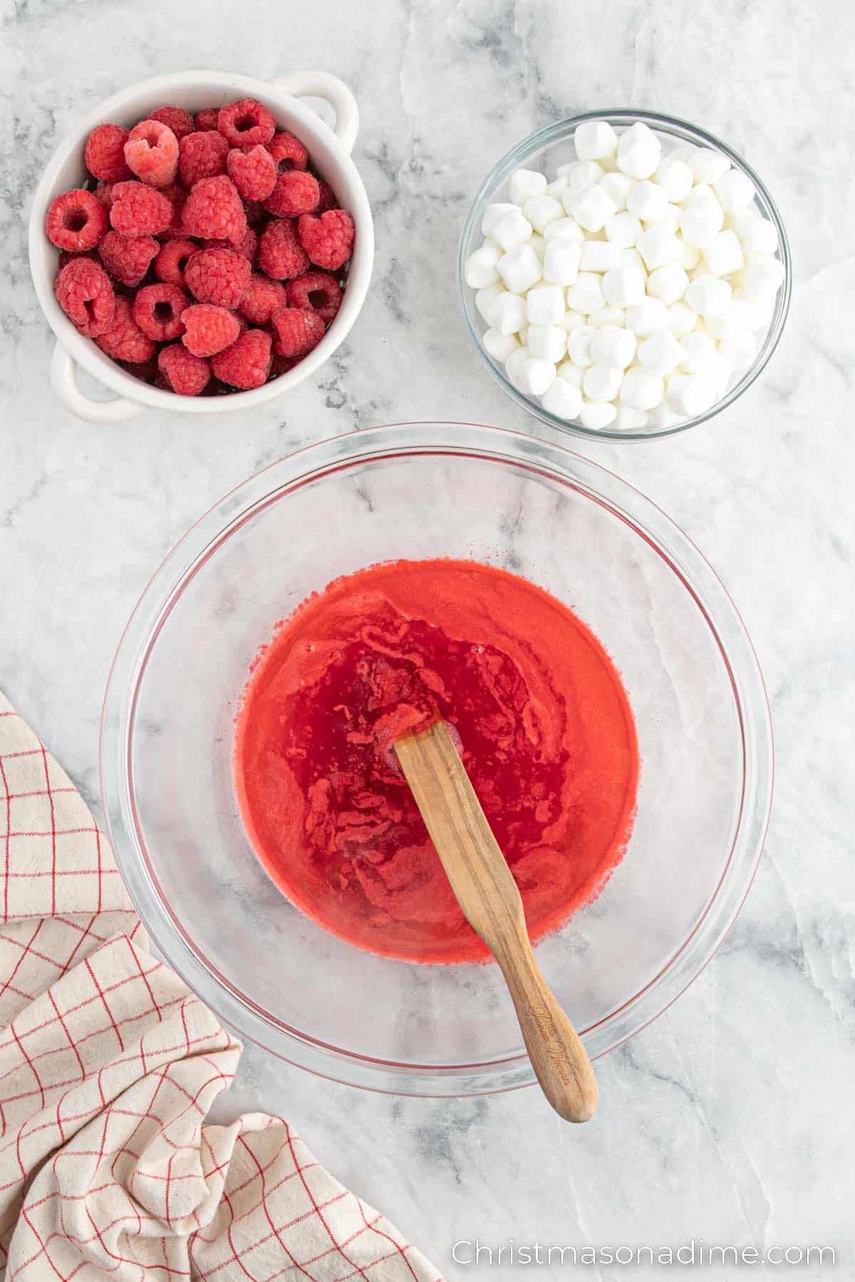 Jello Mixture in a bowl with small bowls of raspberries and marshmallows