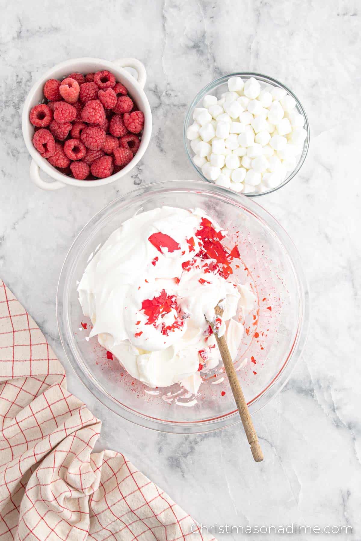 Whipped cream and sour cream mixed together in a bowl with raspberries and marshmallows on the side