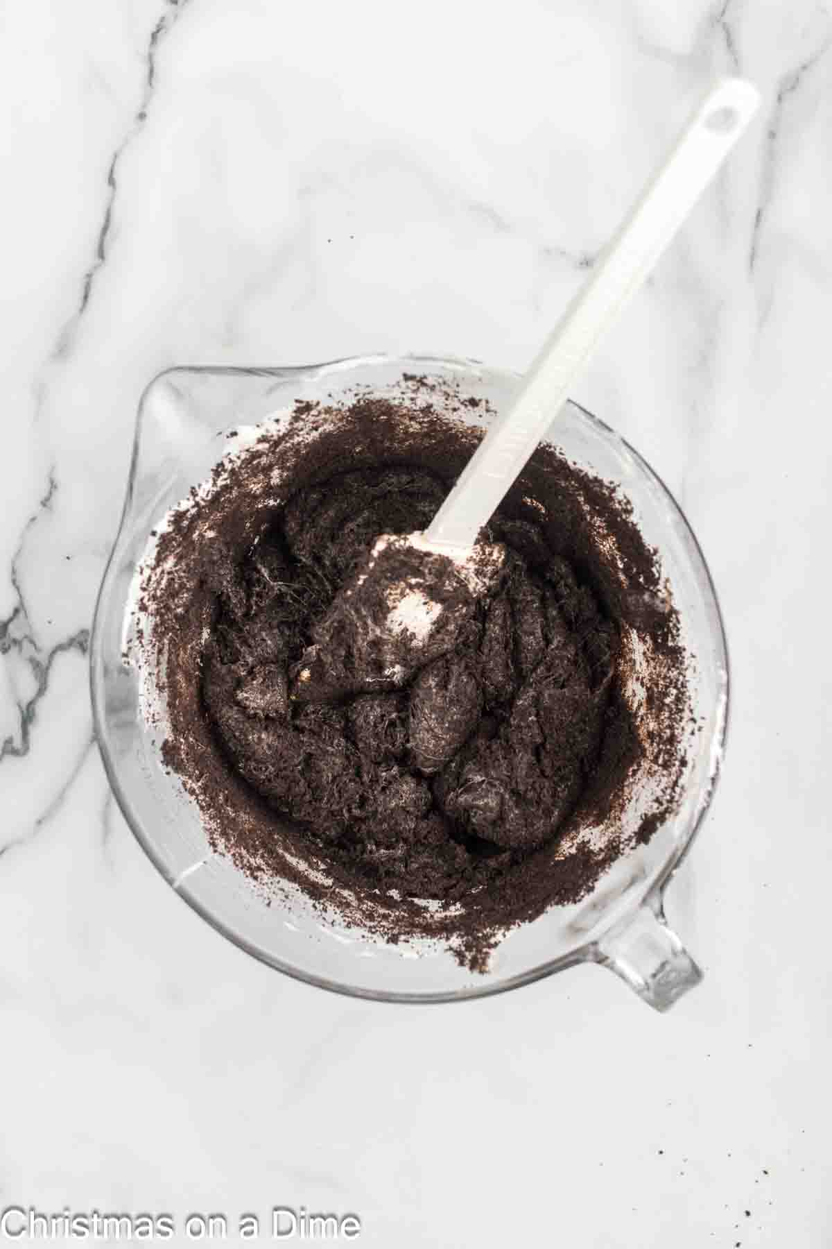 Combining the crushed Oreos into the melted marshmallow mixture in a bowl with a spatula